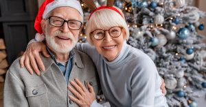 Portrait of happy smiling senior couple in santa hats celebrating at home; blog: Living with Kidney Disease During the Holidays