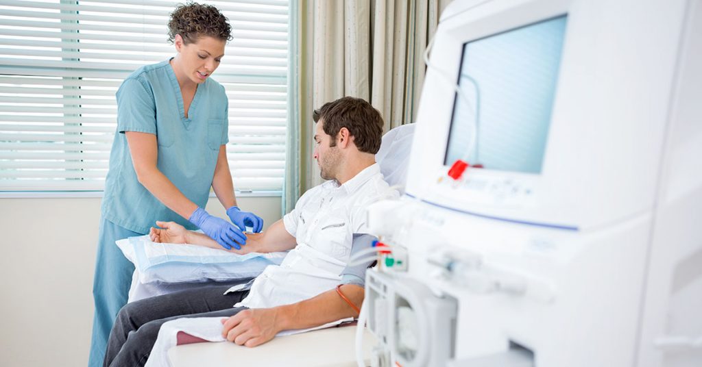 Mid adult female nurse injecting patient for renal dialysis treatment in hospital room; blog: what is hemodialysis?