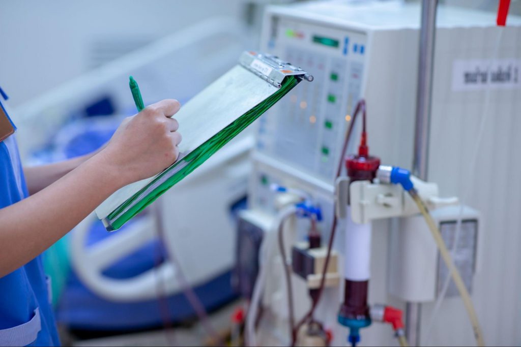 a nurse taking notes in front of a dialysis machine