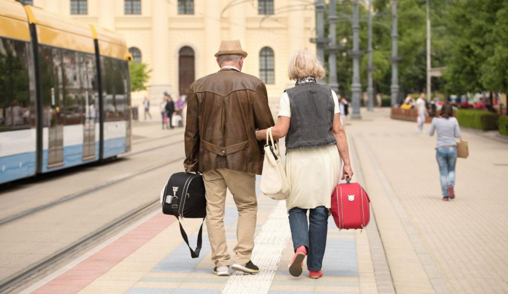an elderly couple walking alongside a train to represent traveling with a medical condition