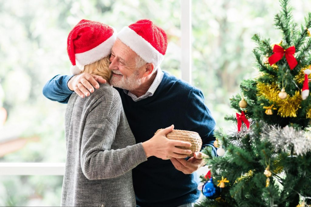An elderly couple embracing next to a Christmas tree to represent Kidney Care Over the Holidays